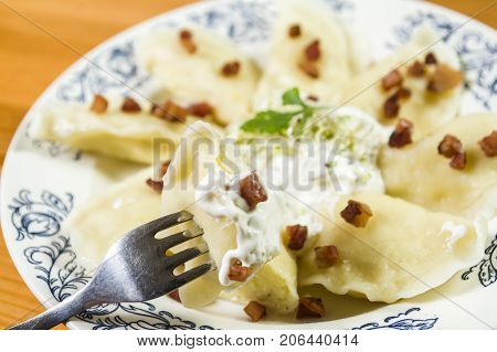 Cooked dumplings with cheese pork scratching and creme fraiche on wooden table. Polish ukrainian russian traditional food.