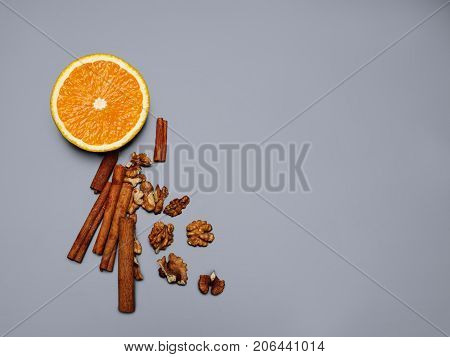 Walnuts, delicious fresh orange and cinnamon sticks are depicted on a gray background. Copy space. Close-up of objects.