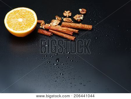 Walnuts, delicious fresh orange and cinnamon sticks are depicted on dark gray background. Copy space. Close-up of objects.