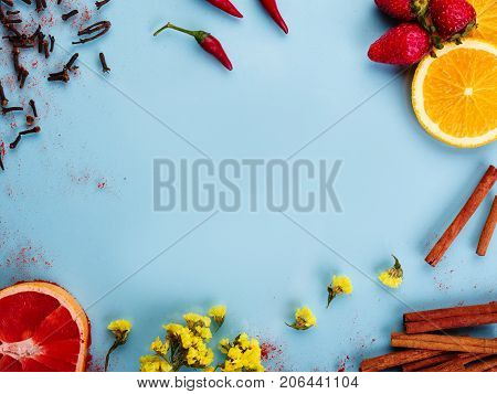 Bright multicolored objects on a blue background. Orange, red grapefruit, red chile, cinnamon sticks, chamomile and wildflow. Copy space fot text.