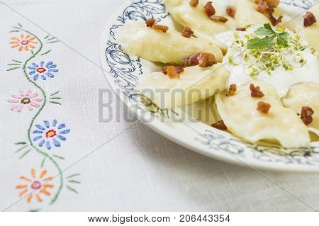 Cooked dumplings with cheese pork scratching and creme fraiche on wooden table. Polish ukrainian russian traditional food.