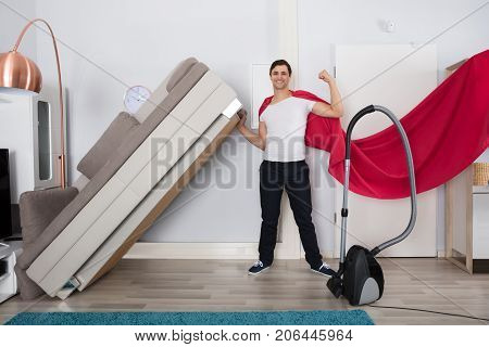 Portrait Of A Smiling Superhero Man Lifting The Couch With Woman