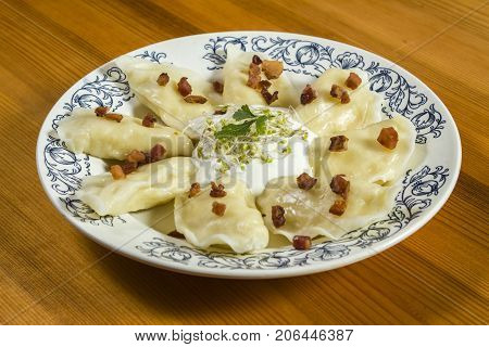 Cooked dumplings with cheese pork scratching and creme fraiche on wooden table. Polish ukrainian russian traditional food.