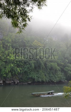 Longboat and morning fog on the river Kwai in Kanchanabury province, Thailand