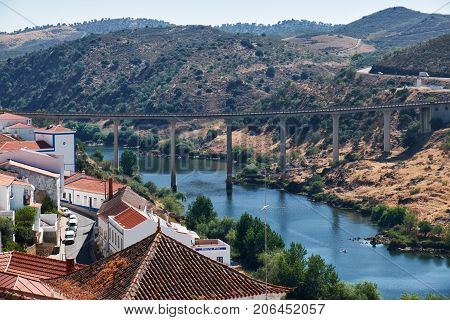 MERTOLA PORTUGAL - JUNE 30 2016: The view of bridge across the valley of Guadiana river with residential houses of Mertola on the foreground. Mertola. Portugal