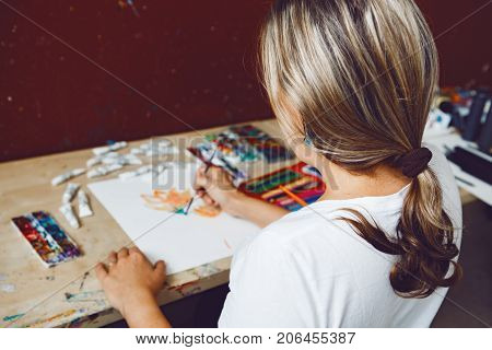 Portrait of Caucasian female artist painting flowers with watercolor paints and colored pencils. Woman painter at work in art studio. Lifestyle and hobby concept