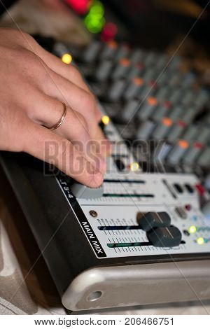 DJ working on a audiomixer at a nightclub. Close-up of hands adjusting quality of music using a knobs of the audio mixer