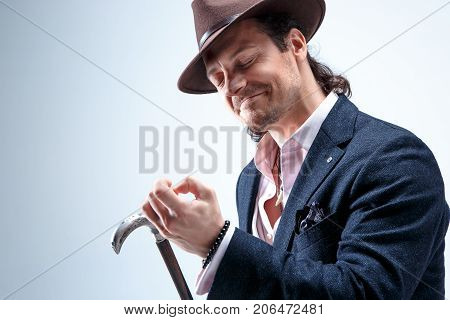 The mature bearded man in a suit and hat holding cane. Isolated on a gray studio background.