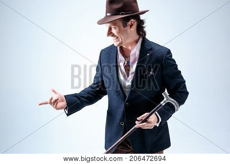 The mature bearded man in a suit and hat holding cane. Isolated on a gray studio background.