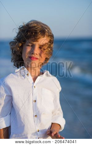 Portrait of boy of 10-11 years against the background of the rough sea. Sea wind ruffled the blond curly hair of the boy. Boy is dressed in a white shirt.