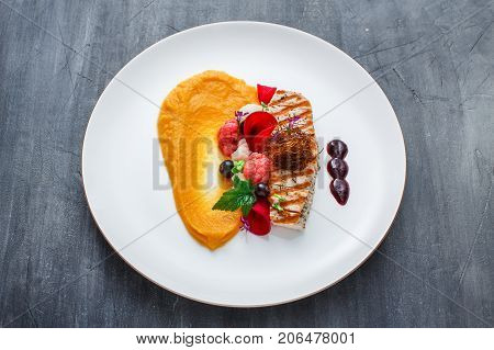 Grilled turkey fillet with pumpkin puree and vegetables on white plate. Close view