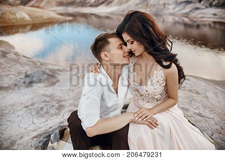 Beautiful Couple In Love Kissing And Hugging Sitting On The Rocks Amid The Fabulous Mountains. Red B