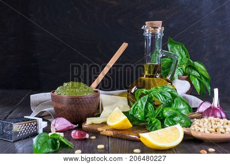 Tradizione Italiana Homemade Pesto recipe ingredients on dark table. Parmesan cheese, basil leaves, pine nuts, olive oil, garlic.