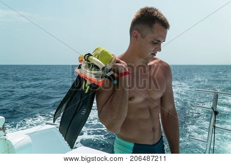 The Guy Stands In The Slats In The Stern Of The Yacht With Fins And A Mask In His Hands. The Guy Is