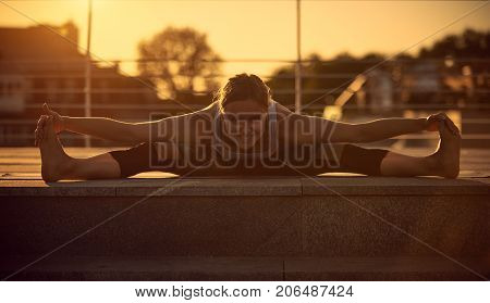 Young attractive woman practicing yoga, sitting in Samakonasana Straight angle posture in the terrace at sunset