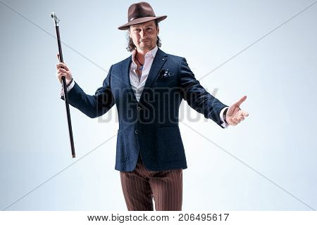 The mature man in a suit and hat holding cane. Isolated on a gray studio background.