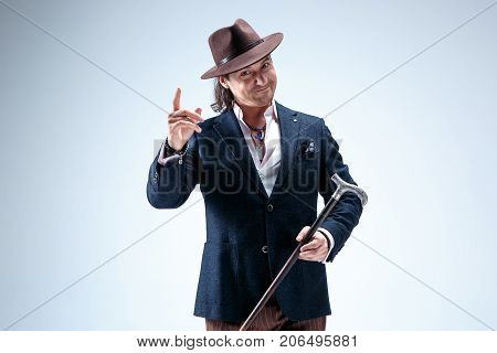 The mature man in a suit and hat holding cane. Isolated on a gray studio background.
