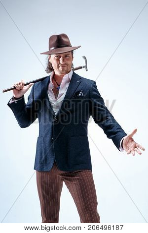 The mature man in a suit and hat holding cane. Isolated on a gray studio background.