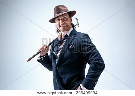 The face of young man portrait with hat on gray studio background. The retro man holding cane