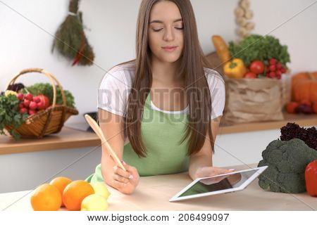 Young  woman is making online shopping by tablet computer and credit card. Housewife found new recipe for  cooking in a kitchen.