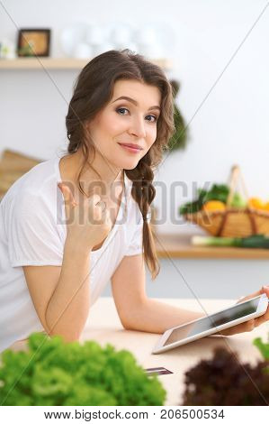 Young  woman looking for a new recipe for  cooking in a kitchen. Housewife is making online shopping by tablet computer and credit card.