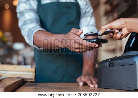 Closeup of a customer using her smartphone and nfs technology to pay a for her purchase at a cafe