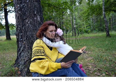 family mom and daughter reading a book in the woods