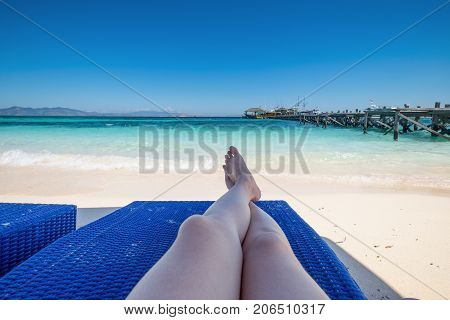 Sence view of the beach with a woman sitting on the blue chair. Relaxing and enjoying on summer vacation at sea.