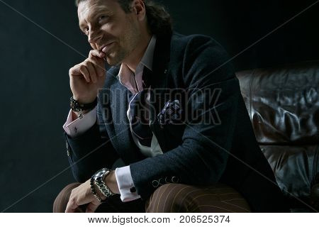 The mature stylish man in a suit on a gray studio background. Businessman sitting on an armchair