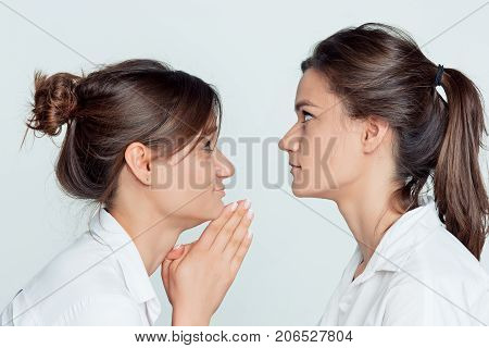 Studio profile portrait of young female twins sisters on gray