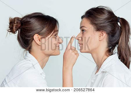Studio profile portrait of young female twins sisters on gray