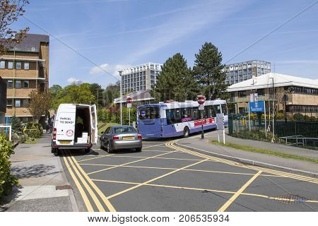 Swansea, UK: May 04, 2016: Traffic congestion and a white delivery van parked on double yellow lines at Singleton Hospital. A bus is passing through the barrier between the hospital and university