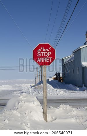 Octagon red stop sign with in Inuktitut (Syllabic), English and French snow on the ground