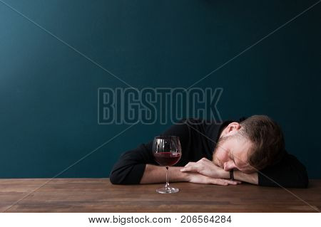 Drunk young male sleeping in bar. Unlucky date. Problems in adult ife, tired man with red wine on blue background with free space. Bad day, trouble in business concept