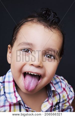 Playful little boy sticking out his tongue with smiling eyes over a dark background