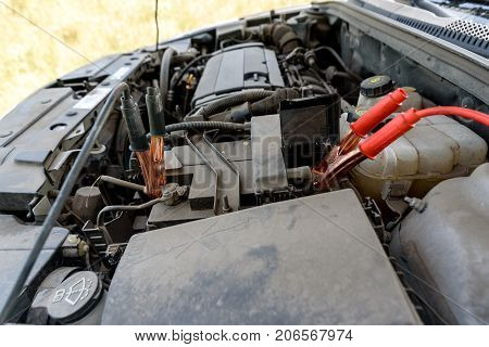 Jumper Cables Charging Battery On Car. Red And Black Car Battery Booster Cables. Charging Car Batter