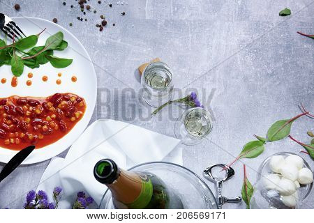 Top view of a white plate with drops of sauce and fresh green leaves, bay leaves, a half of juicy yellow lemon, little-speckled quail eggs, a jar with different seasonings on a light gray background.