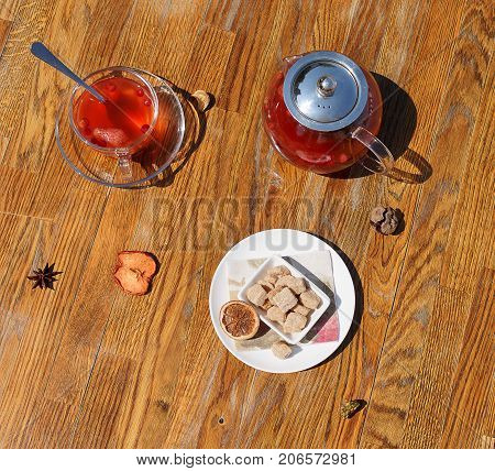 Top view of a nutritious winter breakfast on a brown wooden background. A bowl of buttered biscuits and a full glass teapot on a table. A cup of red, hot, berry tea with dried fruits and carnation.