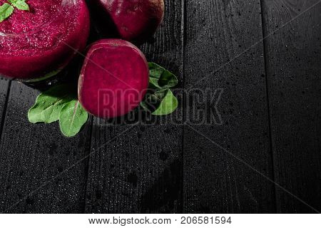 Beautiful dark beetroot cocktail with mint in a transparent glass on a dark wooden background. Natural vegetables and green salads. Healthy restaurant beverages and juices. Copy space.
