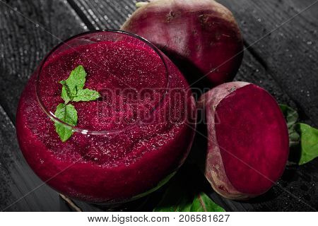 A close-up picture of bright red beet smoothie in a glass on a black table background. Juicy beetroots with fresh salad leaves and green decorative mint. Detoxification and dietary concept.