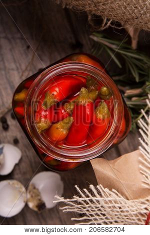 Closeup of red spicy chili papper in a glass jar, green twigs of rosemary and empty speckled shells of quail eggs, indredients for delicious meal on a wooden background.