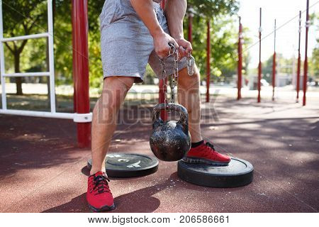 A strong man with sexy body is doing exercises on his feet. A handsome young man lifts weights with his feet in the park.