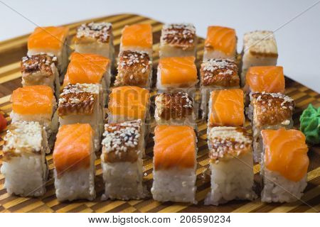The set of rolls with ginger and wassabi on bamboo board. Unagi rolls and philadelphia rolls. Focus on middle line.