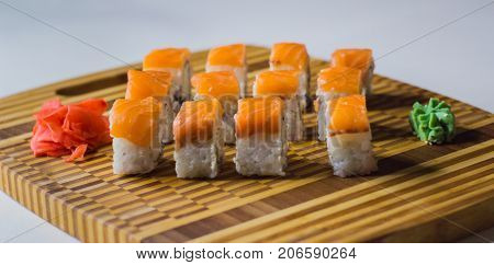The set of salmon rolls on bamboo board with ginger and wasabi.