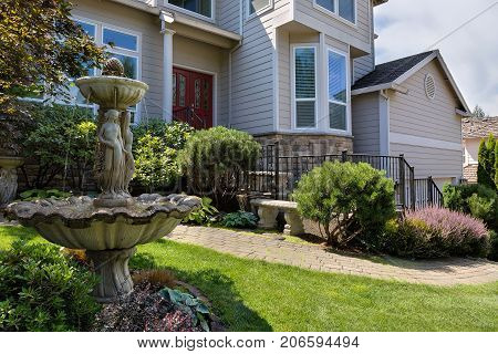 Residential single home in North America suburbs frontyard with manicured garden green lawn paver brick walkway bench and stone water fountain