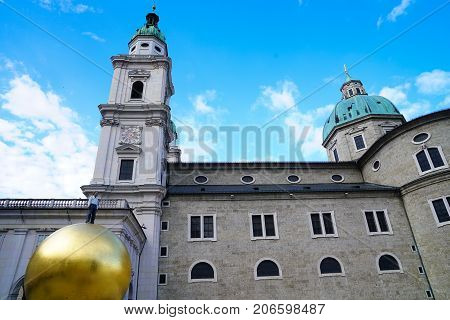 SALZBURG AUSTRIA - SEPTEMBER 6 2017; Cathedral Square or Domplatz with centrepiece giant golden ball with man on top statue with people moving about taking in the historic atmosphereand cathedral background.