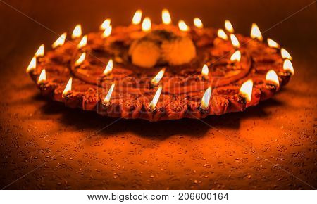 Stock Photo of an illuminated terra-cotta Diwali lamp or Diya with detailed artwork on it. on a moody background and selective focus