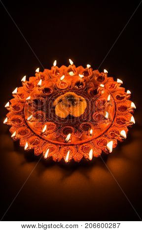 Stock Photo of an illuminated terra-cotta Diwali lamp or Diya with detailed artwork on it. on a moody background and selective focus