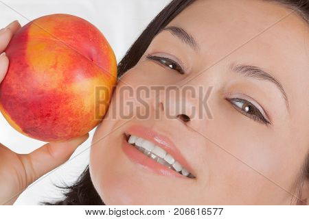 Perfect Skin Concept. Beautiful Girl Holding a Peach Near Her Face on a white background