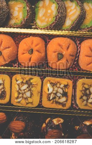 stock photo of Indian sweet or mithai and oil lamp or diya with gift box and flowers on decorative or colourful background, selective focus